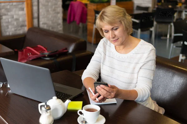 Una mujer con un portátil trabaja en un café, mira las redes sociales . — Foto de Stock