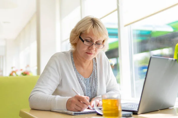 Uma mulher com um laptop olha para um documento em um café, escritório — Fotografia de Stock