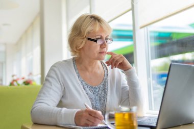 Bilgisayarlı bir kadın bir kafede, ofiste bir belgeye bakıyor.