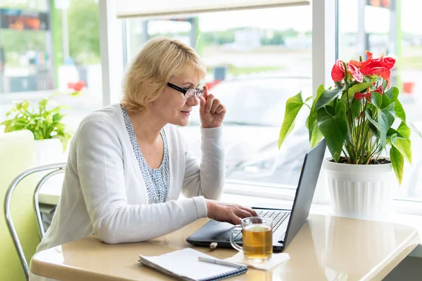 Uma mulher com um laptop olha para um documento em um café, escritório — Fotografia de Stock