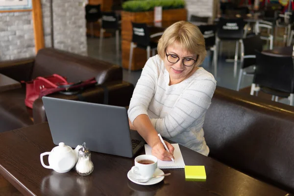 Μια γυναίκα με λάπτοπ δουλεύει σ 'ένα καφέ, βλέπει κοινωνικά δίκτυα.. — Φωτογραφία Αρχείου