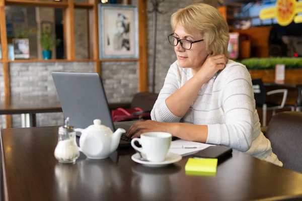 Uma mulher com um laptop trabalha em um café, ela assiste redes sociais . — Fotografia de Stock