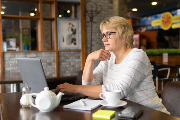 Una mujer con un portátil trabaja en un café, mira las redes sociales . — Foto de Stock