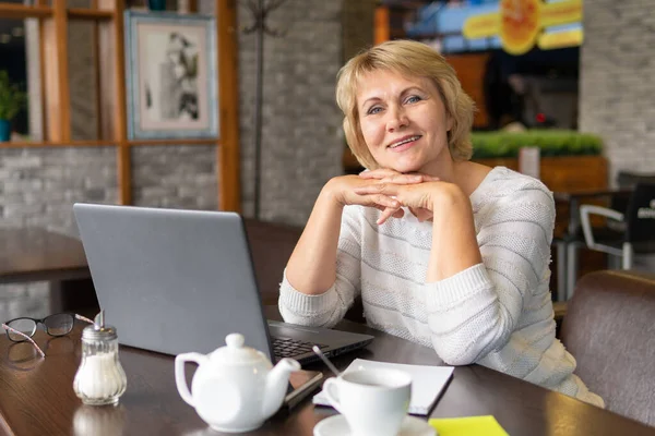 Uma mulher com um laptop trabalha em um café, ela assiste redes sociais . — Fotografia de Stock