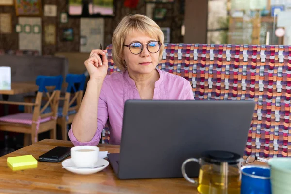 A woman with a laptop works in a cafe, she watches social networks.