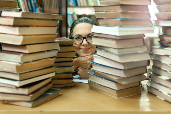 Μια γυναίκα στη βιβλιοθήκη μπροστά από τα ράφια. Έννοια της εκπαίδευσης — Φωτογραφία Αρχείου