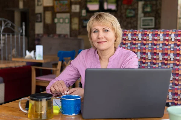 En kvinna med en bärbar dator arbetar på ett café, hon tittar på sociala nätverk. — Stockfoto