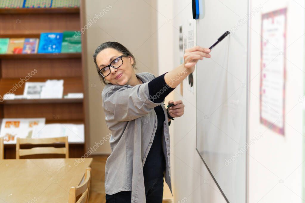 a female entrepreneur or teacher writing on a blackboard with an erasable presentation marker in a conference room.