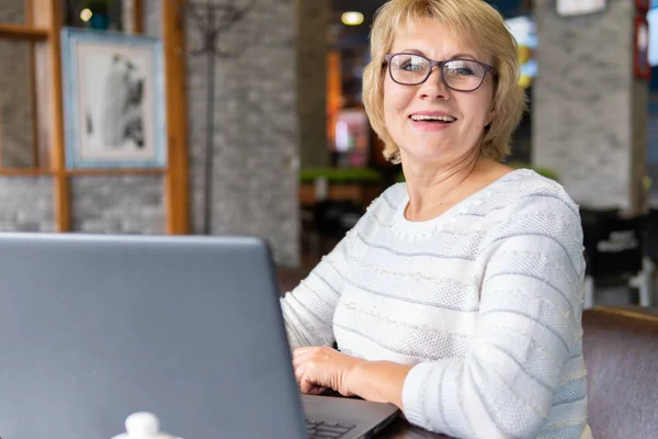 Una donna con un computer portatile guarda un documento in un caffè, ufficio — Foto Stock