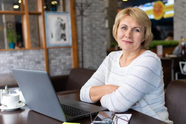 Uma mulher com um laptop olha para um documento em um café, escritório — Fotografia de Stock