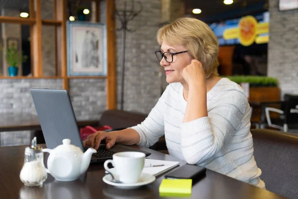 Bilgisayarlı bir kadın bir kafede, ofiste bir belgeye bakıyor.