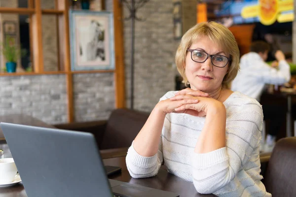 En kvinna med en bärbar dator tittar på ett dokument i ett café, kontor — Stockfoto