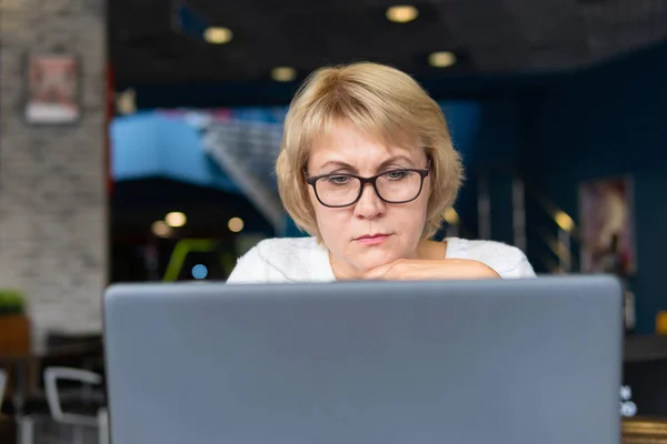 Μια γυναίκα με φορητό υπολογιστή κοιτάζει ένα έγγραφο σε ένα καφέ, γραφείο — Φωτογραφία Αρχείου