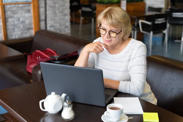 A woman with a laptop looks at a document in a cafe, office — Stock Photo, Image