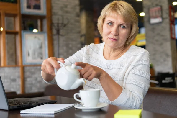 Una mujer con un portátil mira un documento en un café, oficina — Foto de Stock