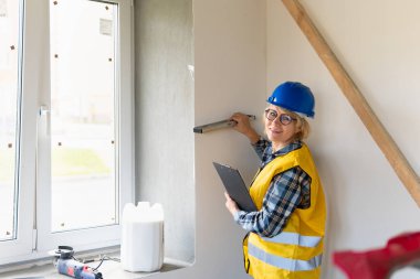 Bir kadın inşaat işçisi ölçümleri kontrol eder. Kasketli orta yaşlı bir kadın dairede tamirat yapıyor..