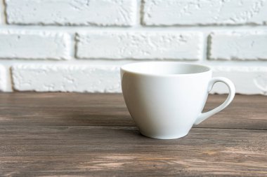 Beyaz boş bardak beyaz tuğla duvara karşı masada. Boşluğu kopyala