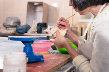 Bir kadın stüdyo atölyesinde kilden yapılmış seramik bir oyuncak yapıyor ve boyuyor..