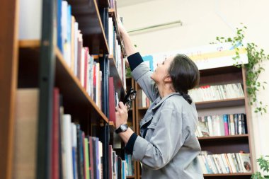 Kütüphanede kitap arayan bir kadın. Orta yaşlı bir kadın kitaplıktaki bir kitaba bakıyor. Yeni yön ve yöntemler öğreniyor..