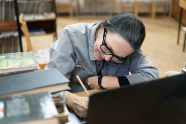 Kütüphanede kitap arayan bir kadın. Orta yaşlı bir kadın kitaplıktaki bir kitaba bakıyor. Yeni yön ve yöntemler öğreniyor..