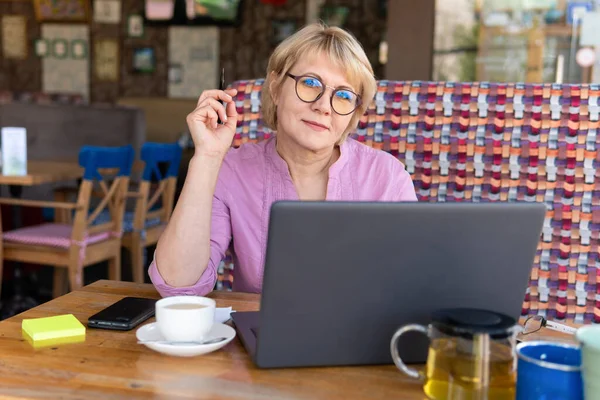 女性はカフェのノートパソコンで働いています 中年の女性がお茶を飲み ソーシャルメディアでニュースを見る 彼女には考えがあった — ストック写真