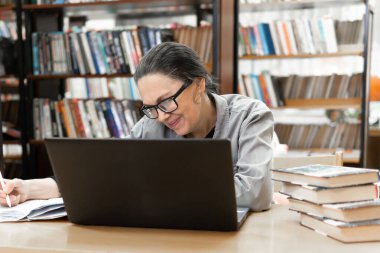 Kütüphanede dizüstü bilgisayarı olan bir kadın. Kitap yığınları olan orta yaşlı bir kadın. Yeni yönleri keşfediyor..