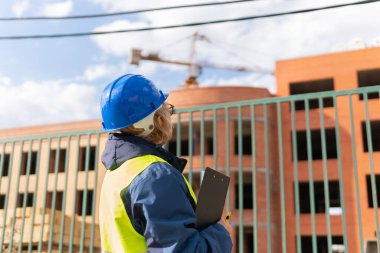 Yeşil yelek ve miğferli bir inşaat alanında kadın inşaat işçisi. Dosyası olan orta yaşlı bir kadın yeni bir evi inceliyor..