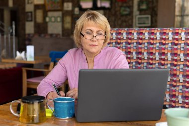 Bir kadın bir kafede, ofiste dizüstü bilgisayarda çalışıyor. Orta yaşlı bir kadın çay içer ve haberleri izler. İnternetten konuşuyor..