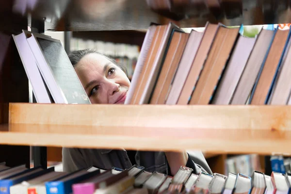 Kütüphanede kitap arayan bir kadın. Orta yaşlı bir kadın kitaplıktaki bir kitaba bakıyor. Yeni yön ve yöntemler öğreniyor..