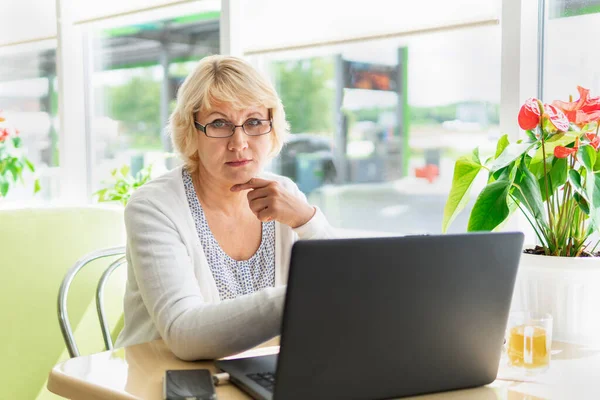 A woman works at a laptop in a cafe. Middle-aged woman drinking tea and watching the news. She\'s a freelancer.