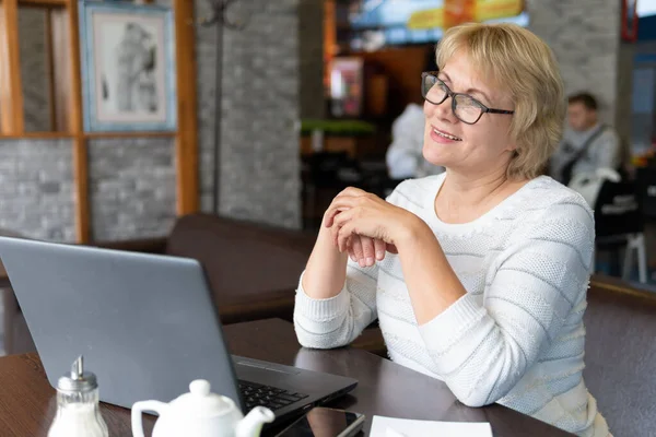 女性はカフェのノートパソコンで働いています 中年の女性がお茶を飲み オフィスでニュースを見ています 彼女はフリーランサーだ — ストック写真