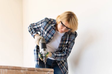 Bir kadın inşaat işçisi duvar kazıyor. Orta yaşlı bir kadın dairede tamirat yapıyor..