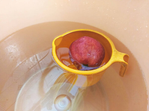 A single red apple placed in a water bucket.