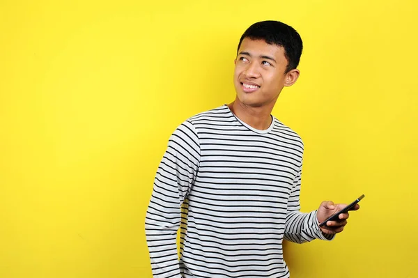 Feliz joven asiático hombre sonriendo con teléfono inteligente mirando a un área en blanco —  Fotos de Stock