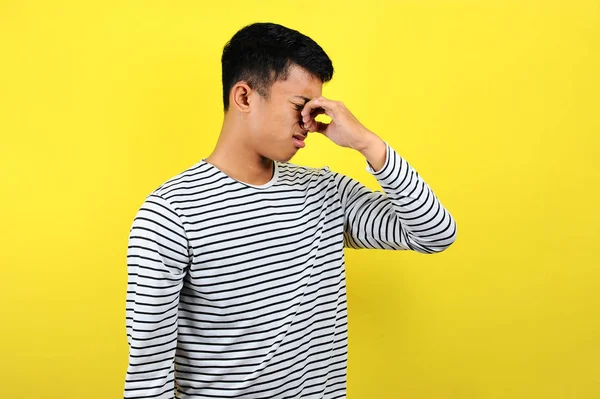 Jovem asiático fechar o nariz para mau cheiro, isolado no amarelo — Fotografia de Stock