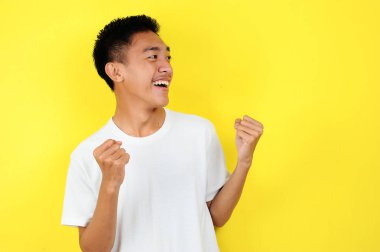 Asyalı genç adam mutlu ve heyecanlı kazanan jestler yapıyor. Başarılı ve sarı ile kutlanıyor.