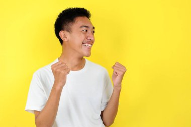 Asyalı genç adam mutlu ve heyecanlı kazanan jestler yapıyor. Başarılı ve sarı ile kutlanıyor.