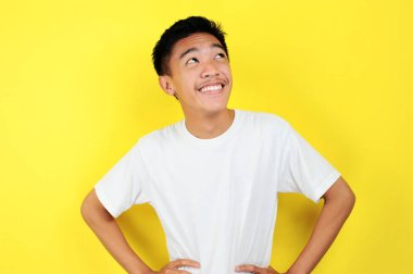 Zeki ve mutlu Asyalı genç bir adamın portresi düşünüp yukarı bakıyor. Mutlu genç Asyalı adam beyaz tişört giyip yukarı bakıyor.