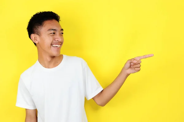 Friendly-looking lively pleasant Asian male with white t-shirt smiling delighted look at copy space joyful. Self-assured pointing — Stock Photo, Image