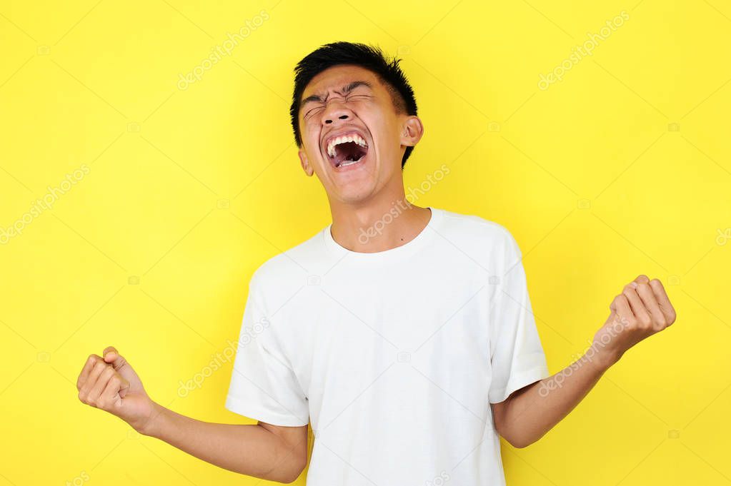 Young asian man happy and excited expressing winning gesture. Successful and celebrating on yellow