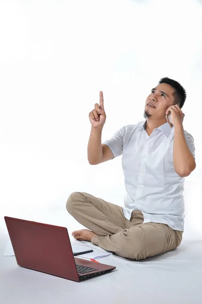 Retrato de empresário asiático sentado no chão branco e chamando o telefone apontado para o espaço de cópia ou área em branco — Fotografia de Stock
