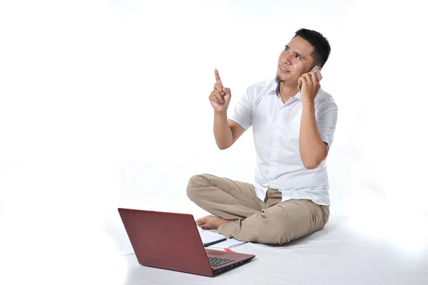 Retrato de empresário asiático sentado no chão branco e chamando o telefone apontado para o espaço de cópia ou área em branco — Fotografia de Stock