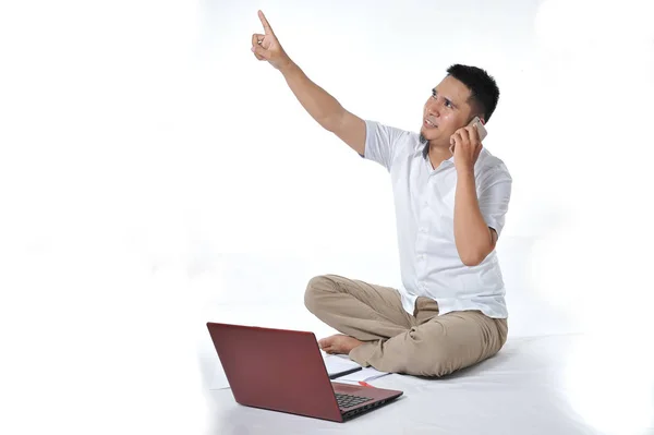 Retrato de empresário asiático sentado no chão branco e chamando o telefone apontado para o espaço de cópia ou área em branco — Fotografia de Stock