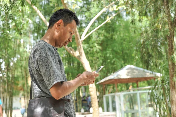Junger asiatischer Mann blickt auf den Bildschirm eines Mobiltelefons. attraktiver junger asiatischer Mann blickt auf den mobilen Bildschirm im Park. — Stockfoto