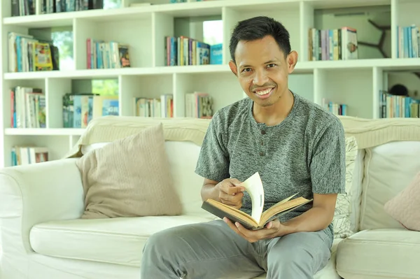 Успішний азіатський чоловік, який фрілансер читає книжку у вітальні. — стокове фото