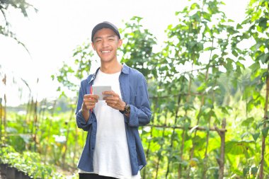 Gülümseyen Asyalı genç çiftçinin elinde defterle mutlu.