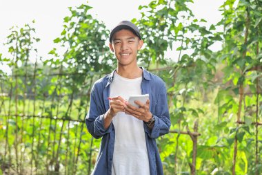 Gülümseyen Asyalı genç çiftçinin elinde defterle mutlu.