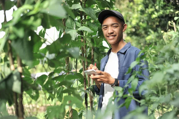 Счастлив улыбающийся молодой азиатский фермер, держащий в руках ноутбук — стоковое фото
