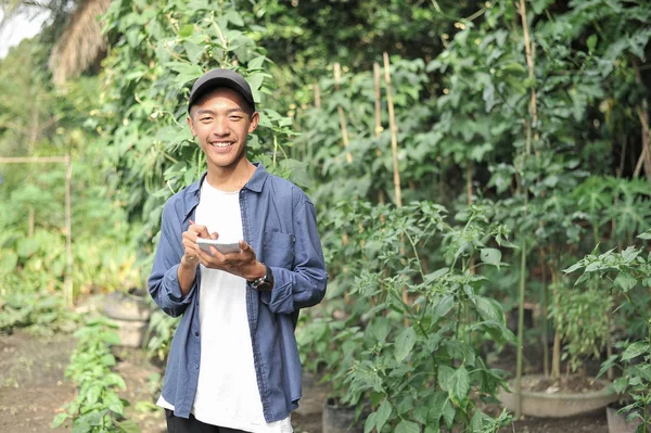 Gülümseyen Asyalı genç çiftçinin elinde defterle mutlu.