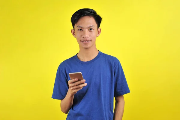 Счастлив молодой красивый азиатский мужчина, улыбающийся при помощи смартфона — стоковое фото